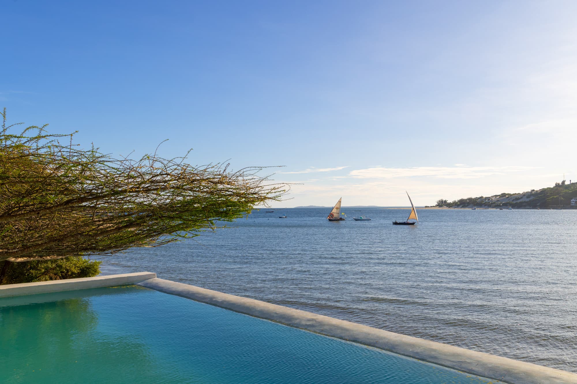 Infinity pool blending into the ocean at dusk with dhows sailing past